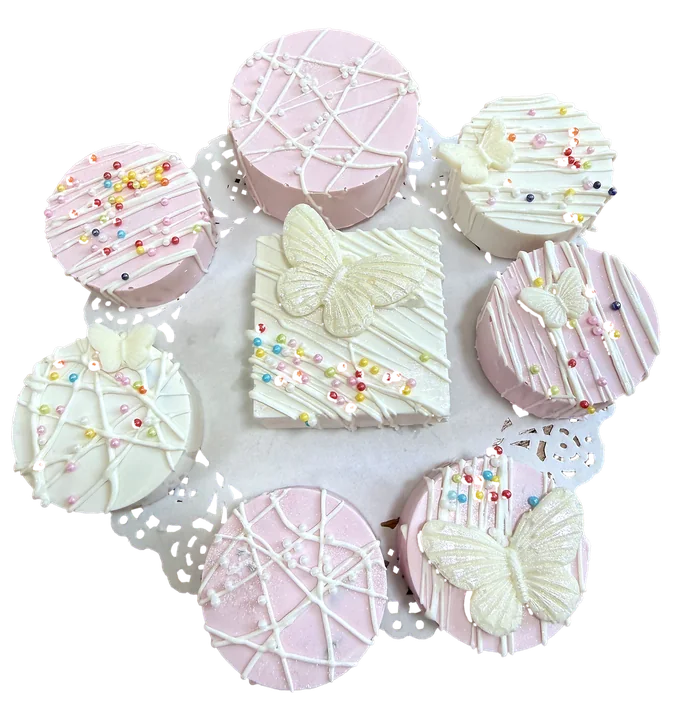 Pink and white chocolate-covered treats with butterflies and rainbow sprinkles on a lace doily